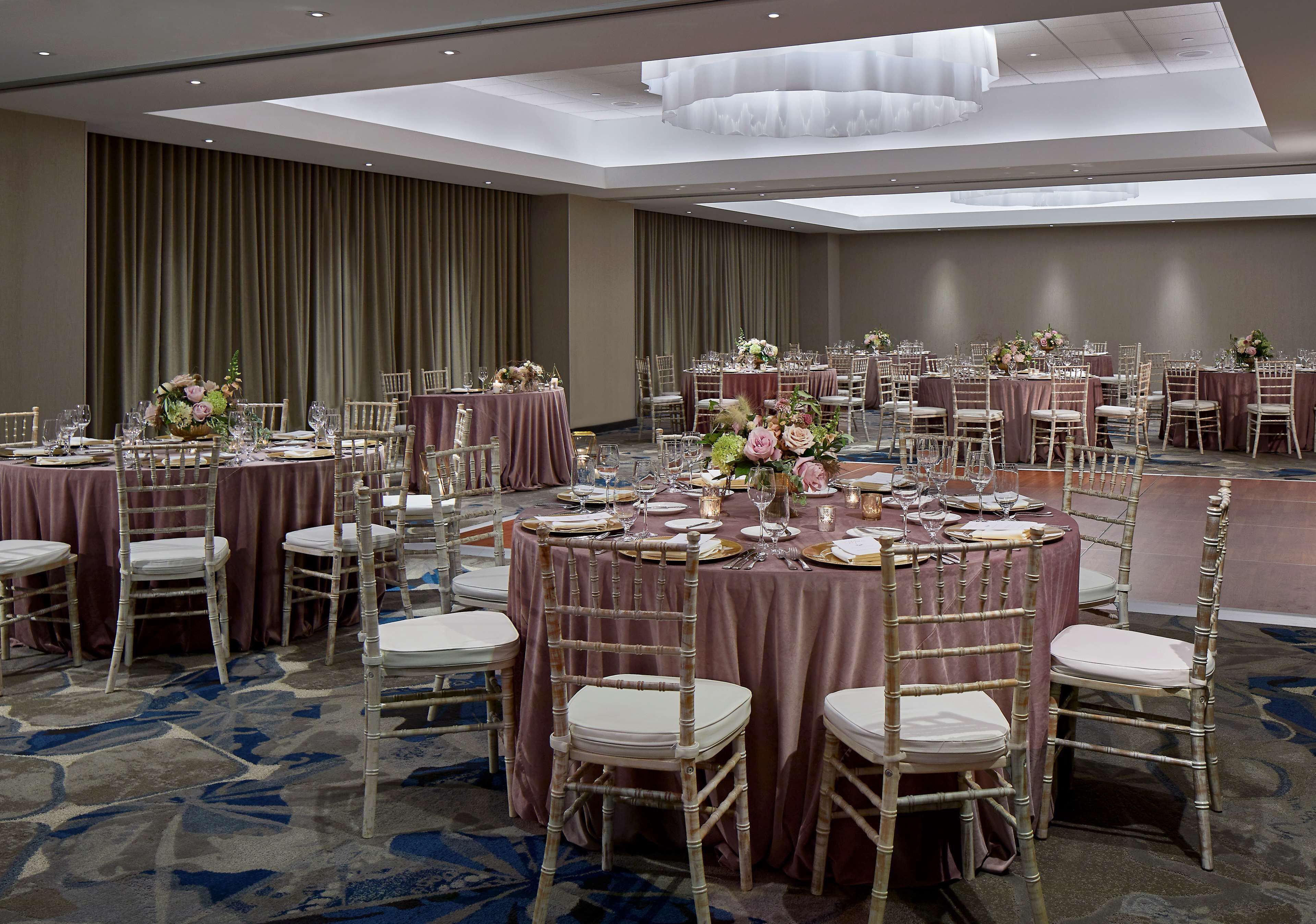A banquet hall with round tables, white chairs, and floral centerpieces.