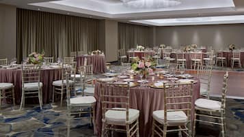 A banquet hall with round tables, white chairs, and floral centerpieces.
