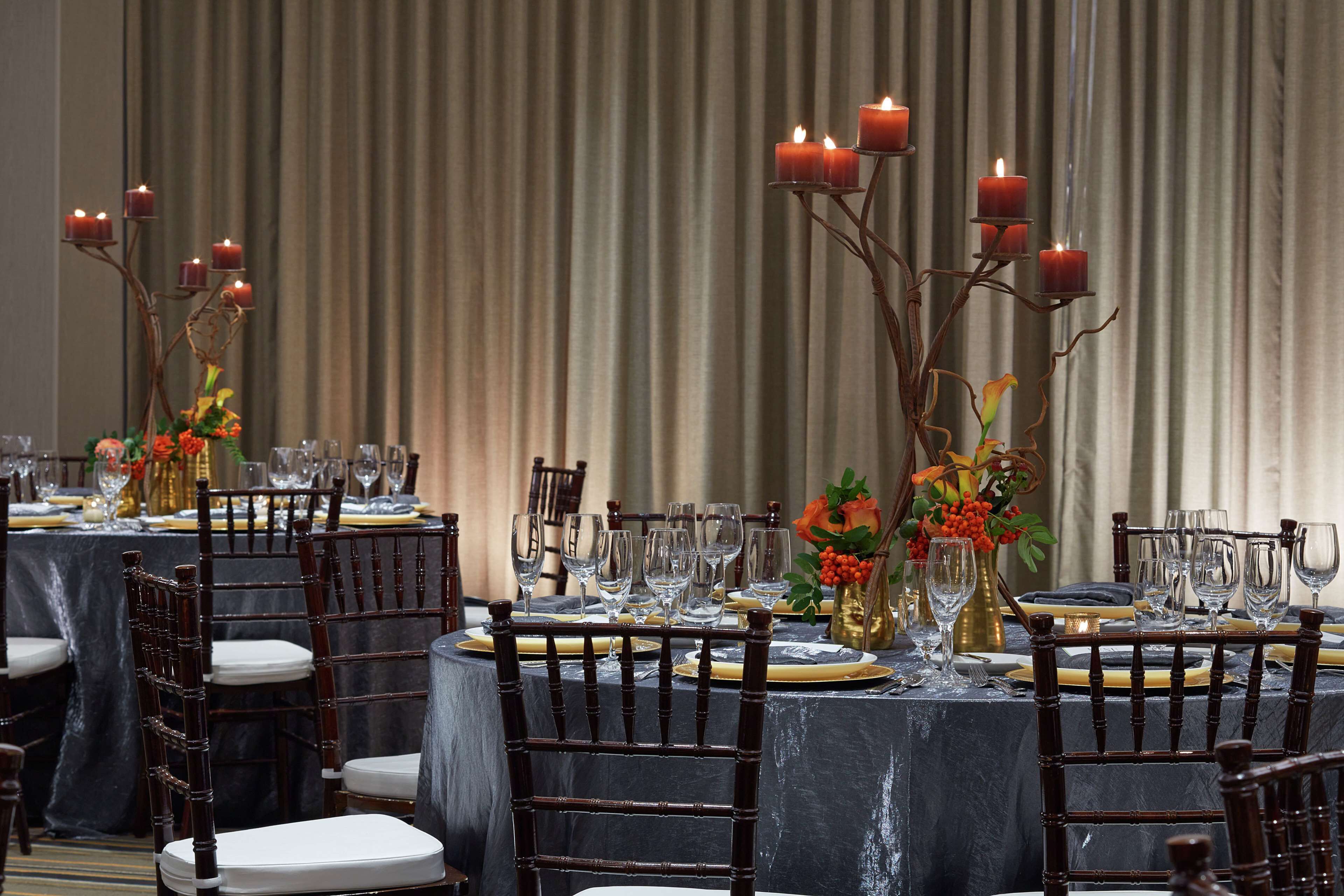 A formal dining setup with tables set for multiple guests, featuring dark wooden chairs, white tablecloths, and candle holders.
