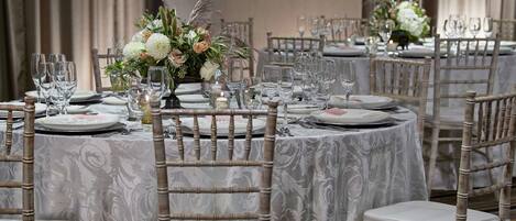 A banquet hall with round tables covered in white tablecloths, each set with plates, glasses, and cutlery.