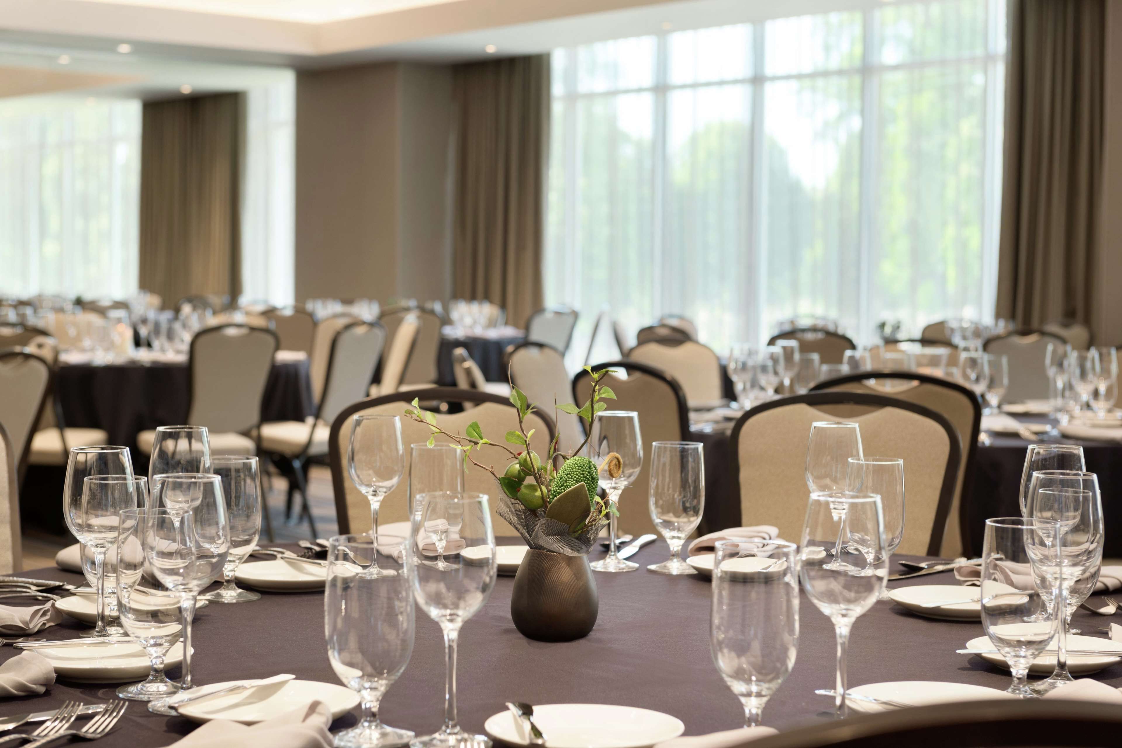 A banquet hall with tables set for a formal event, featuring clear glassware and a central floral arrangement.