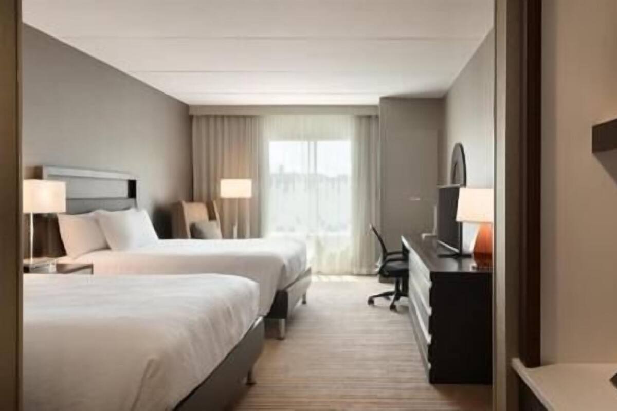 A hotel room with two beds, a desk, a chair, a TV, and a window with curtains.