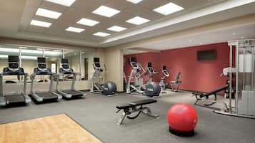 A gym with treadmills, elliptical machines, a bench, and a red exercise ball.