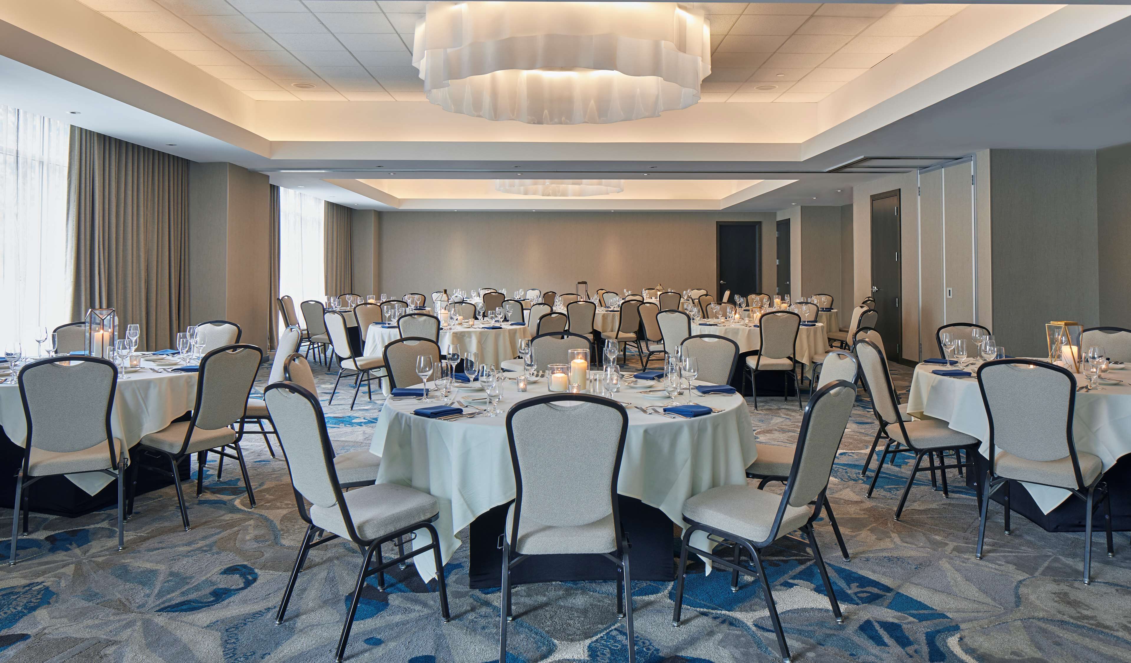 A banquet hall with round tables, chairs, and chandeliers.