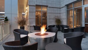 An outdoor patio with a round fire pit surrounded by wicker furniture.