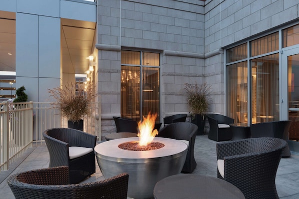An outdoor patio with a round fire pit surrounded by wicker furniture.