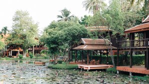 A serene pond with lotus flowers surrounded by wooden structures and lush greenery. - Dhabkwan Resort (Nonthaburi)