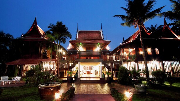 A traditional building with a central courtyard, surrounded by palm trees and a well-lit entrance. - Dhabkwan Resort (Nonthaburi)