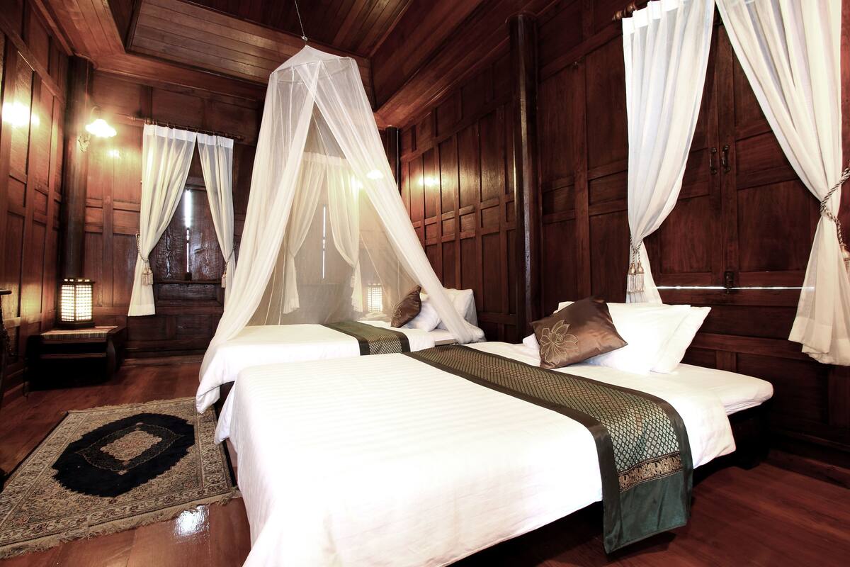 A room with two beds, a wooden floor, and a large window with curtains.
