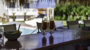 A bar with two drinks, a bowl of fruit, and a view of a pool and greenery. - Stella Maria (Hersonissos)