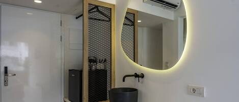 Un bagno moderno con una porta bianca, un lavabo nero e uno specchio tondo con cornice illuminata.