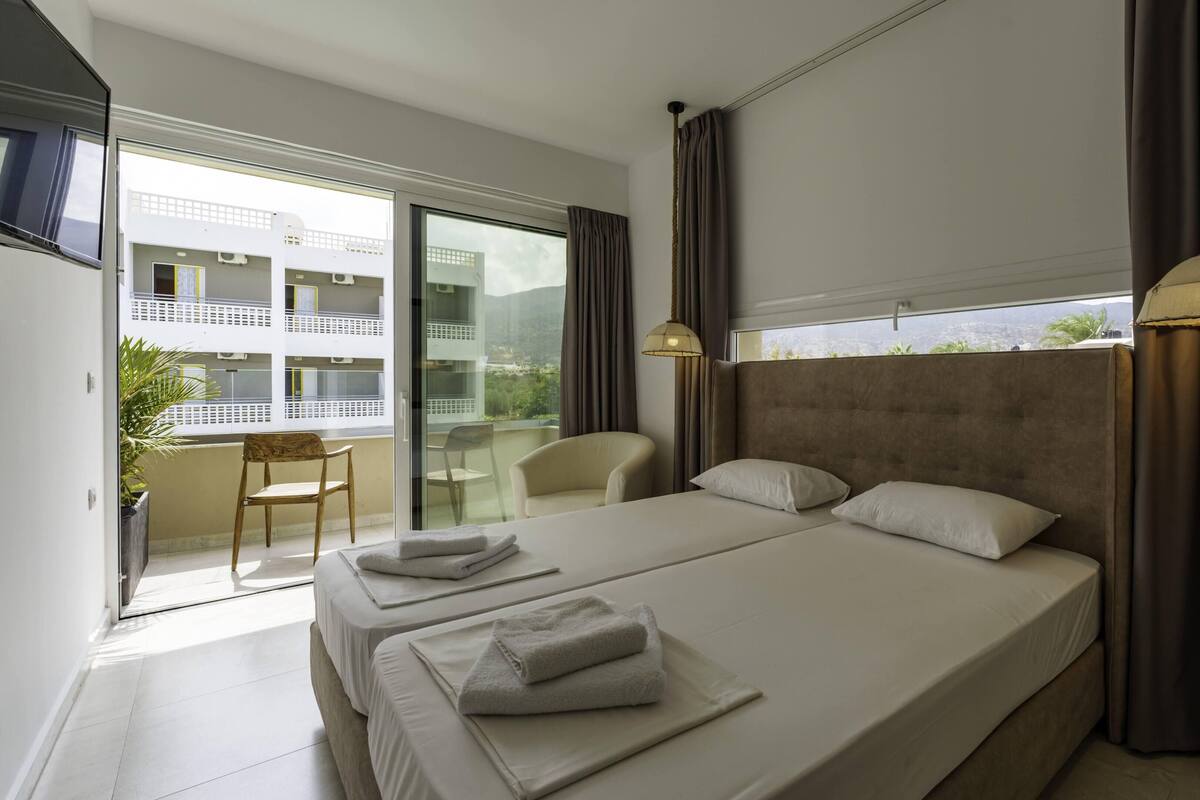Ein modernes Hotelzimmer mit einem großen Bett, zwei Nachttischen, einem Sessel und einem Balkon mit Blick.
