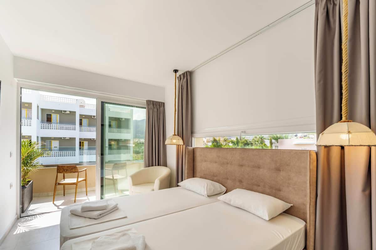 Ein Hotelzimmer mit einem großen Bett, einem Sessel, einem Schreibtisch und Blick auf den Balkon.