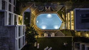 An aerial view of a rooftop pool area with a rectangular pool, surrounded by lounge chairs and umbrellas, set against a backdrop of buildings. - Stella Maria (Hersonissos)