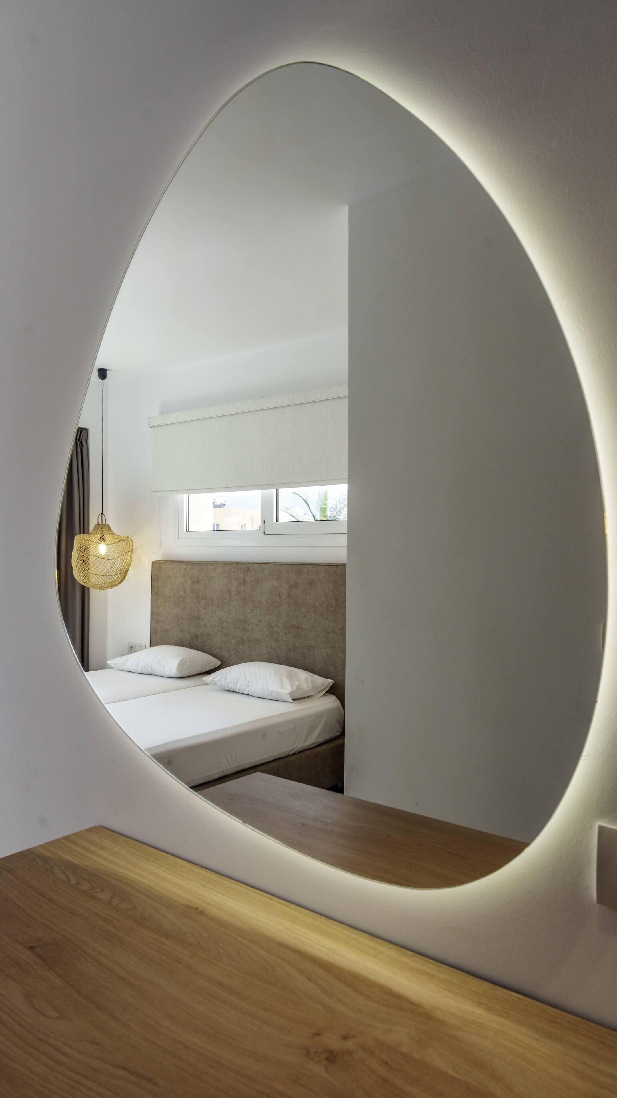 A bedroom with a circular mirror reflecting the bed and window.