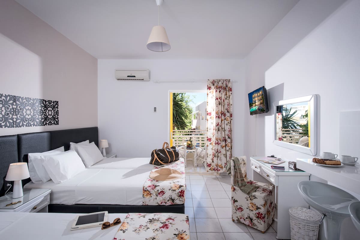 Ein modernes Hotelzimmer mit Bett, Nachttischen, Schreibtisch, Stuhl, Fernseher und einem Fenster mit Blick auf Grünflächen.