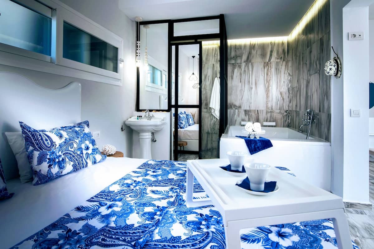 Ein modernes Schlafzimmer mit einem Bett, einem Nachttisch und einem Badezimmer mit Badewanne und Waschbecken.