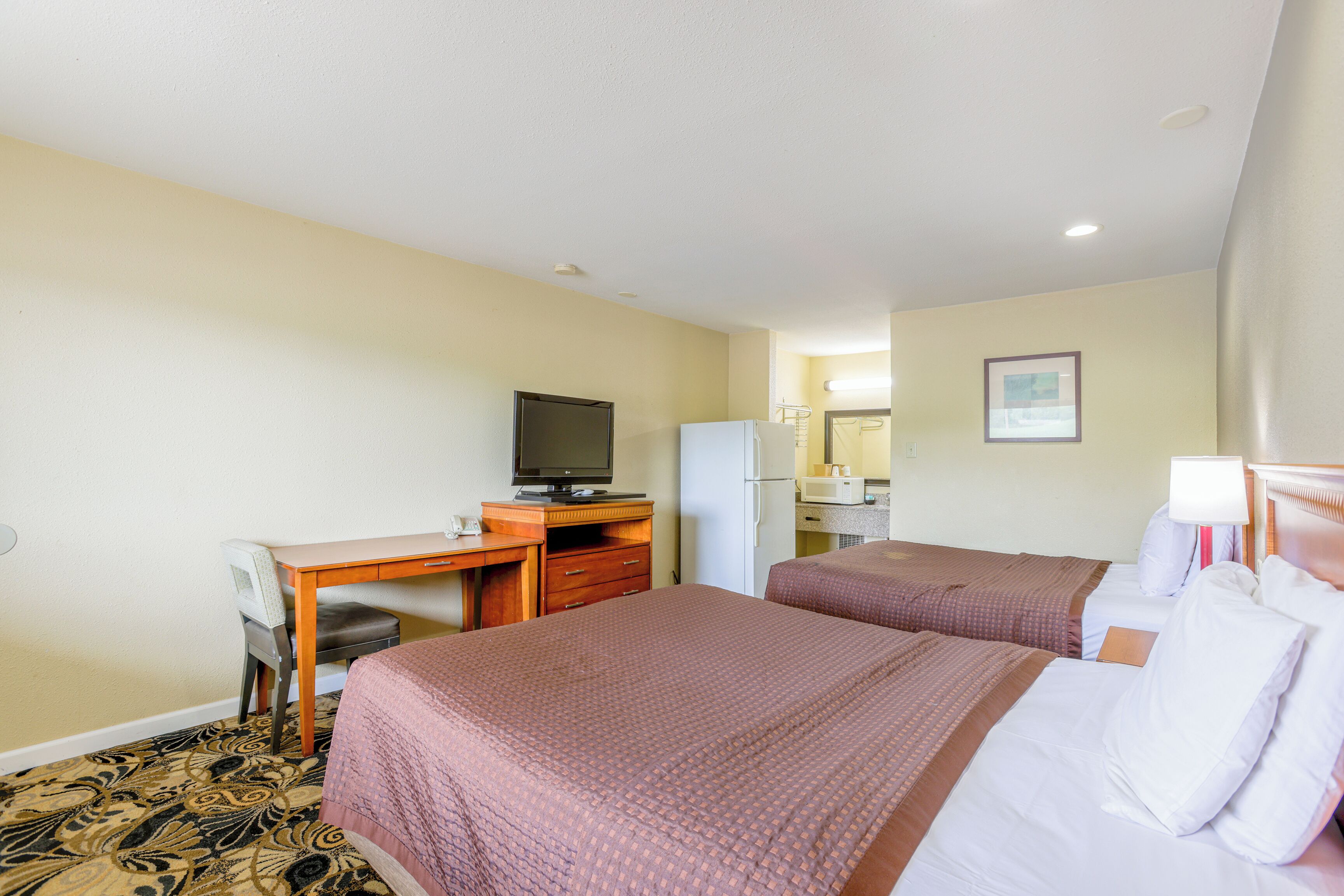 Een hotelkamer met twee bedden, een bureau met een televisie, een koelkast en een magnetron.