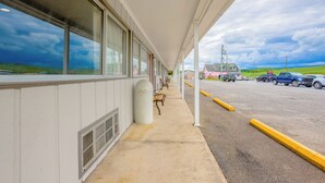 A covered outdoor area with a row of benches, a trash can, and a view of a parking lot with vehicles and a building in the background. - Budget Inn By OYO Natural Bridge I-81 (Natural Bridge)