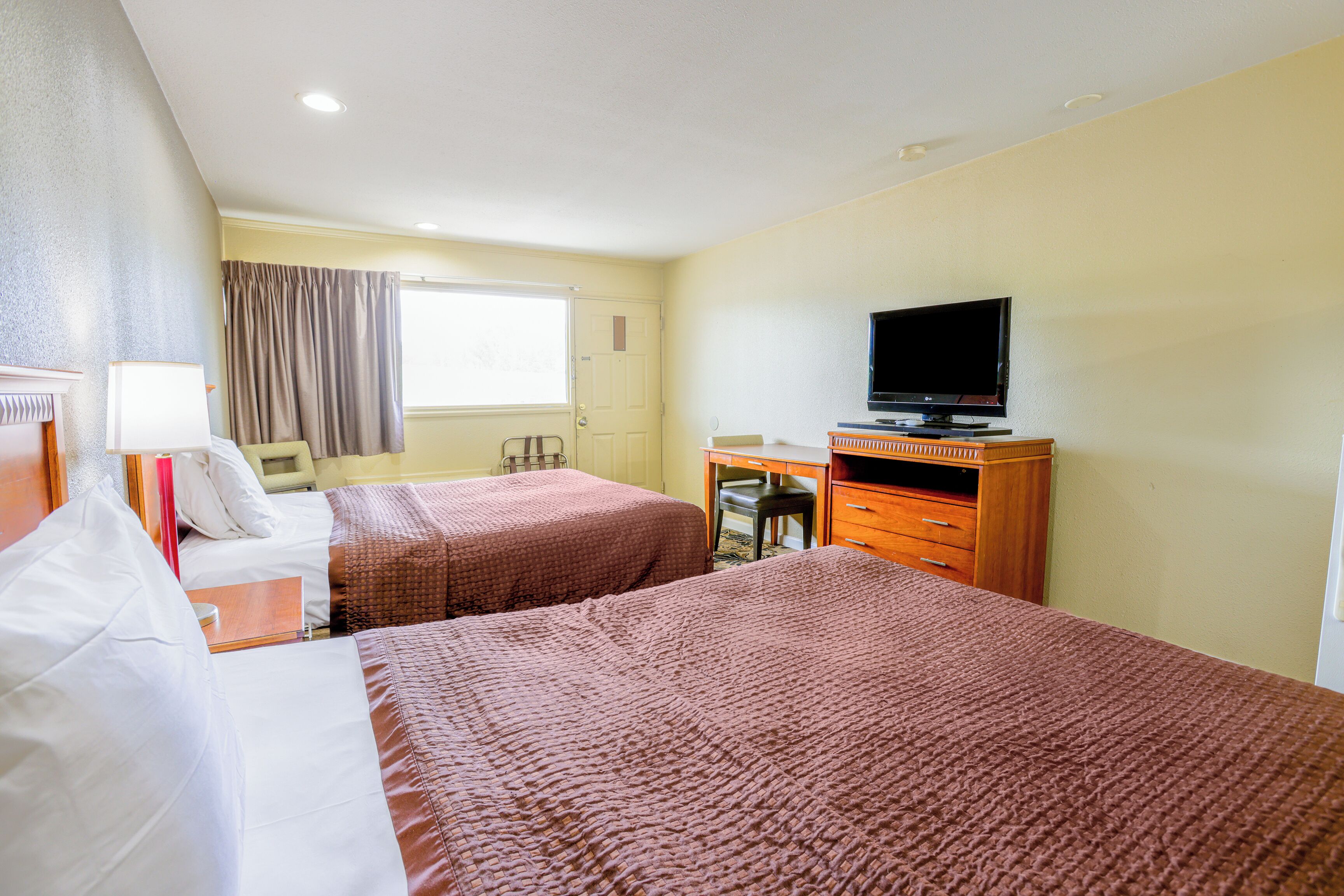 A hotel room with two beds, a desk, a television, and a window with curtains.