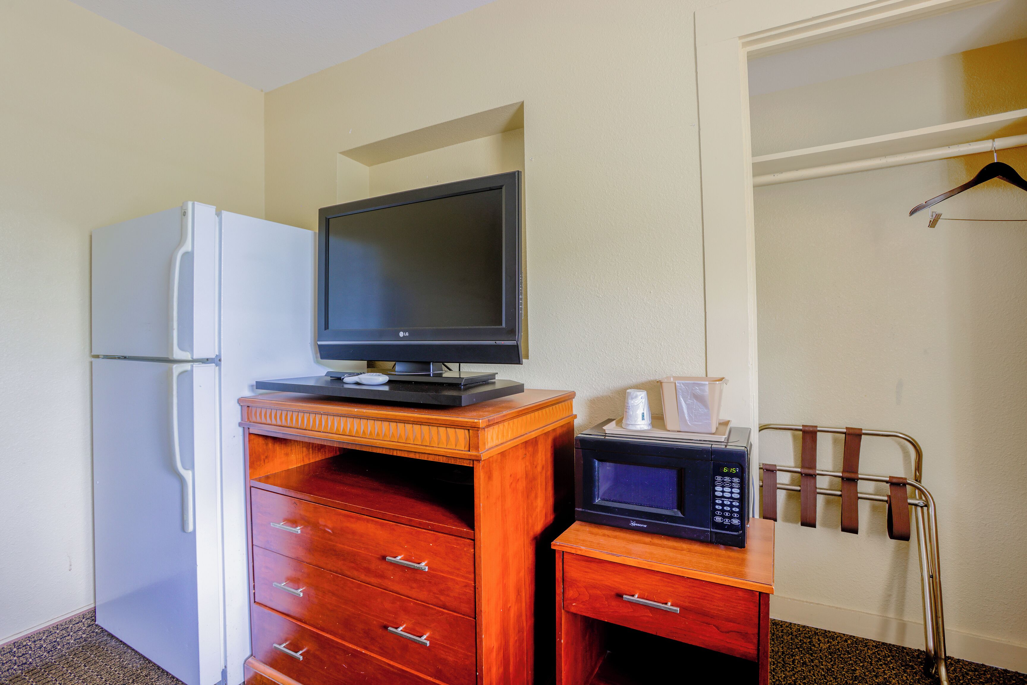 Una kitchenette compacta con un refrigerador blanco, un mueble de madera con cajones, un microondas y un televisor pequeño en la parte superior.