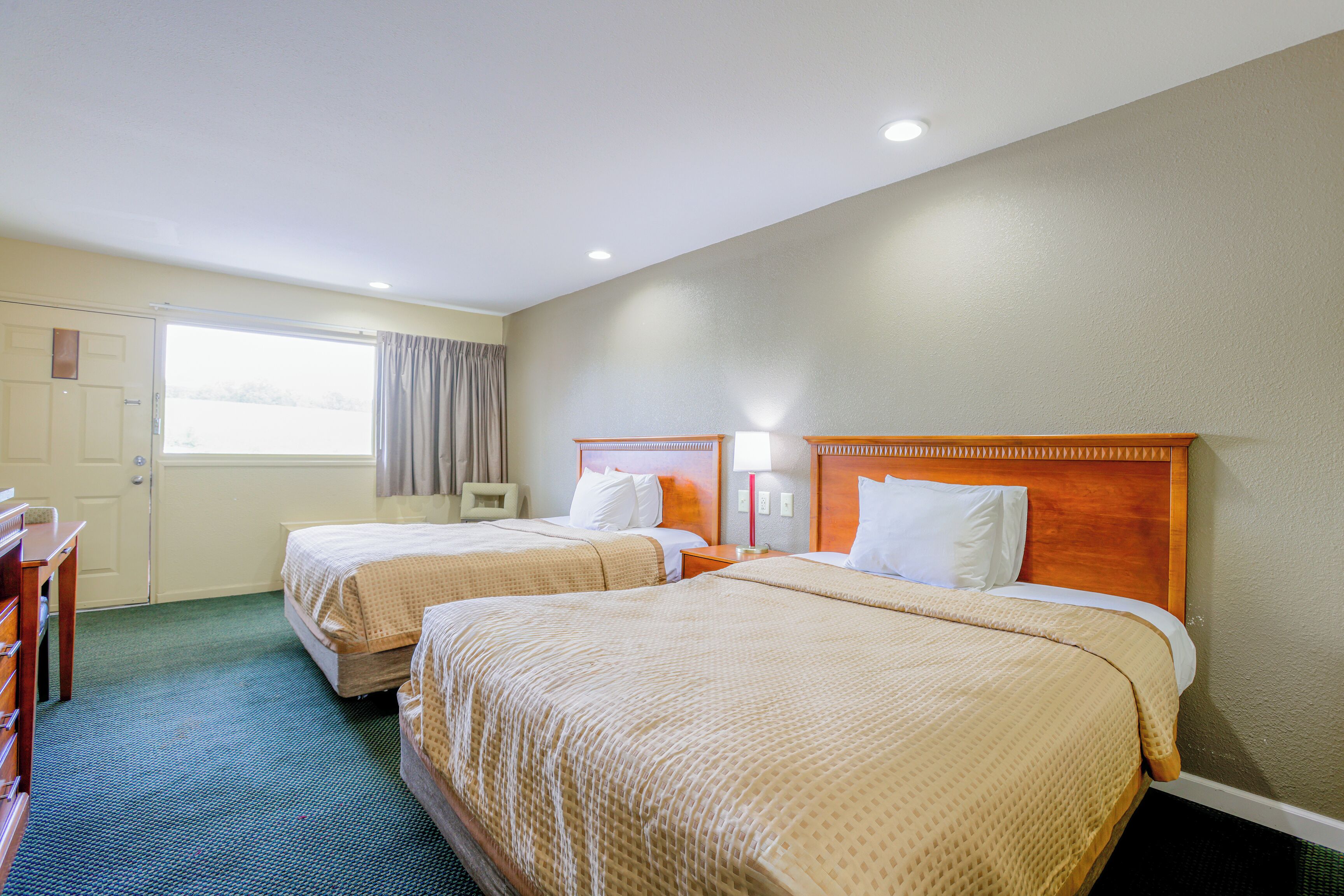 A hotel room with two beds, a wooden headboard, a desk, and a window with curtains.