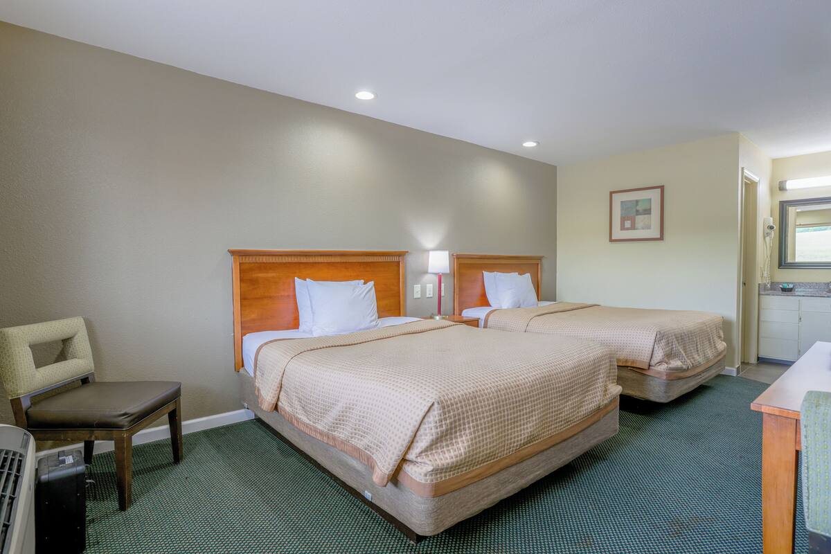 A hotel room with two beds, a chair, a desk, and a kitchenette.