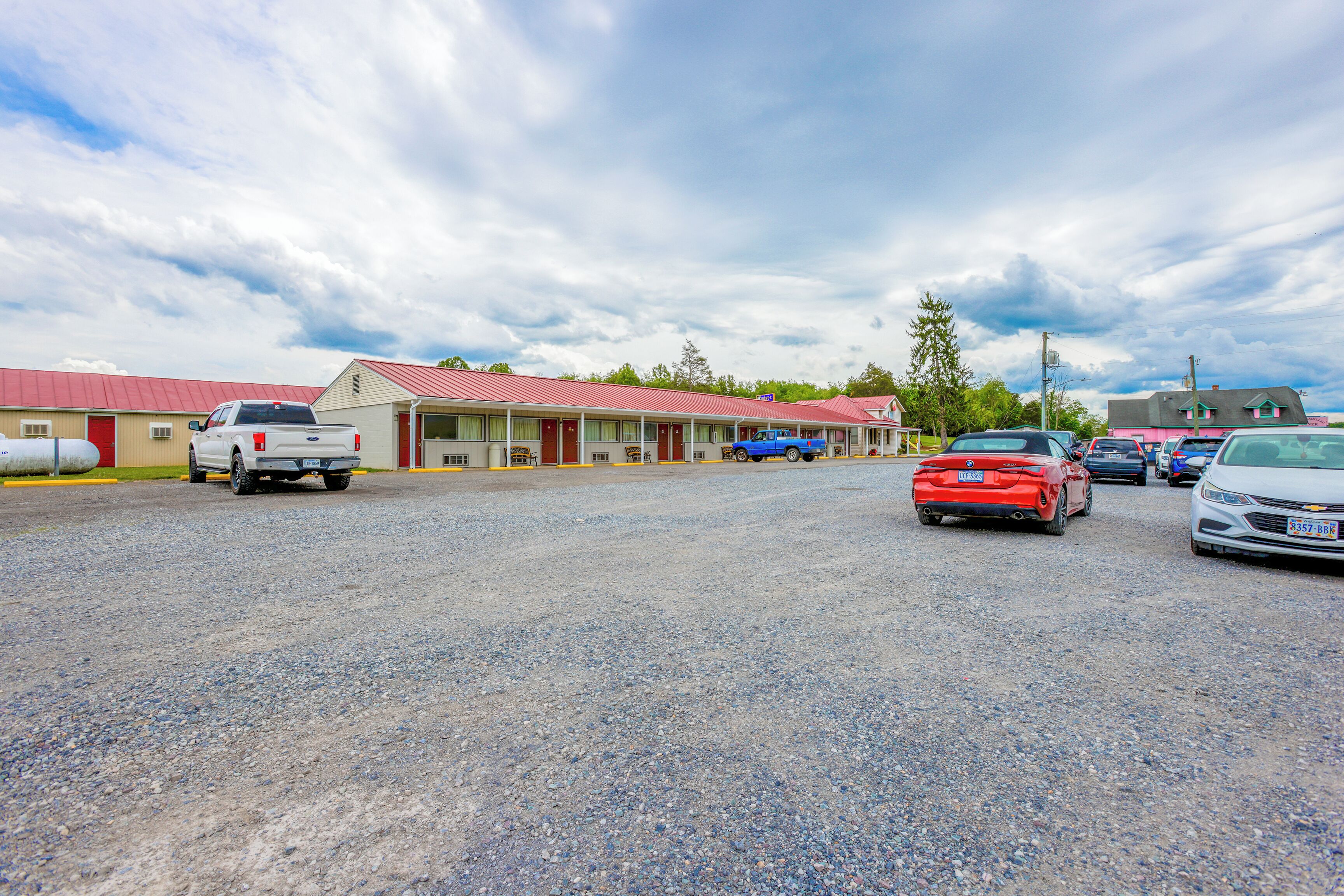 Un motel con estacionamiento de grava, varios coches aparcados y un edificio de techo rojo.