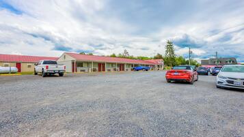 Un motel con estacionamiento de grava, varios coches aparcados y un edificio de techo rojo.