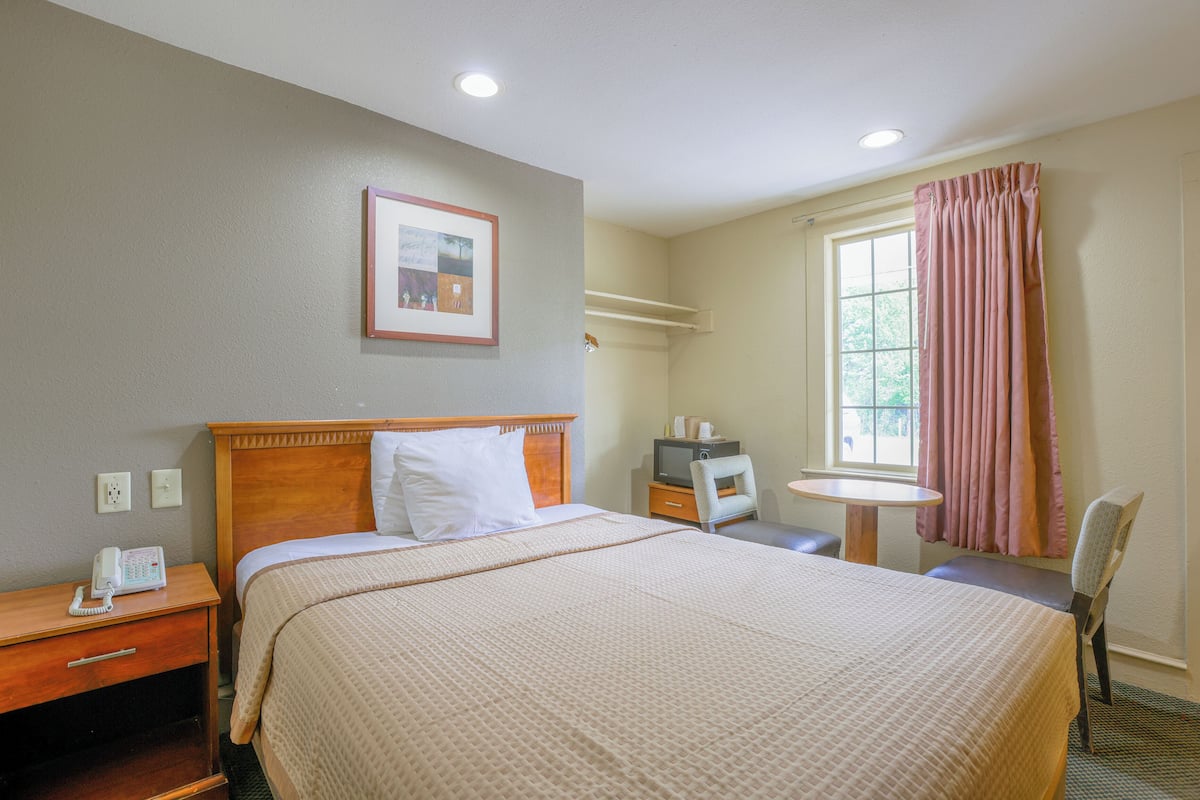 A hotel room with a large bed, bedside table, chair, and a small table with a chair.