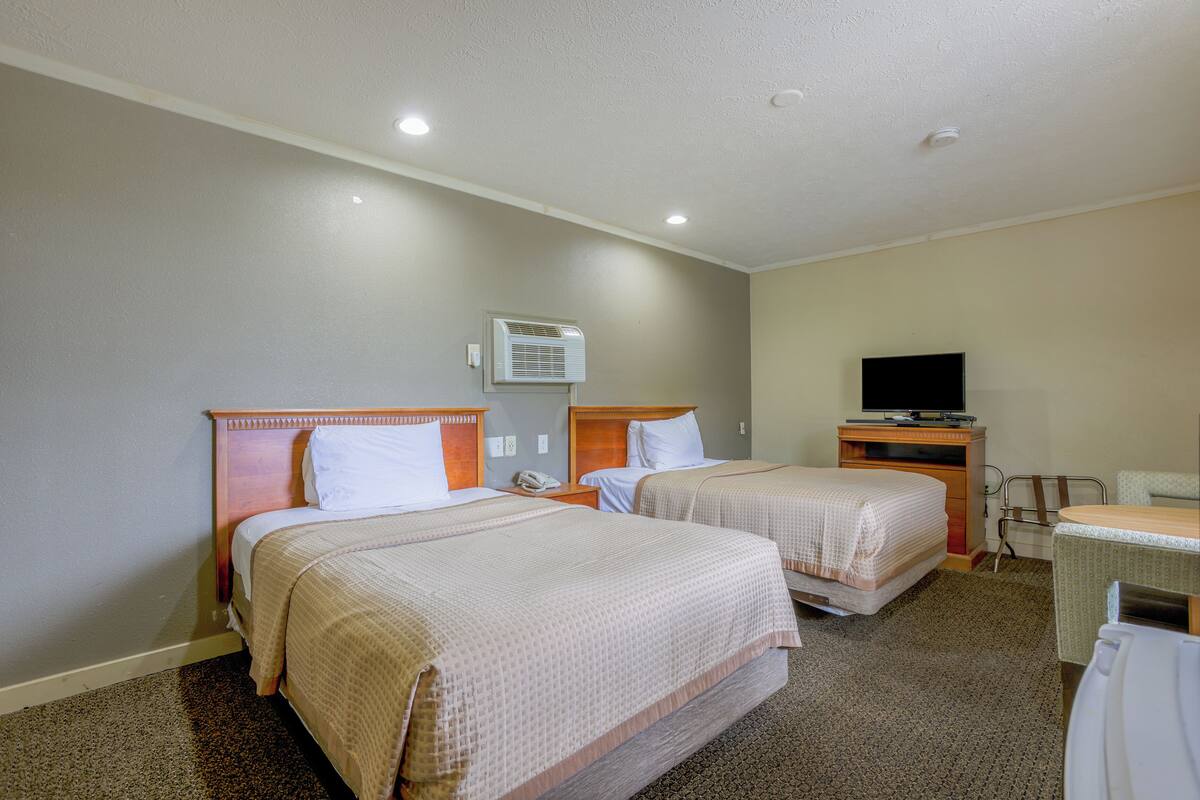 A hotel room with two beds, a desk, a chair, a television, and an air conditioning unit.