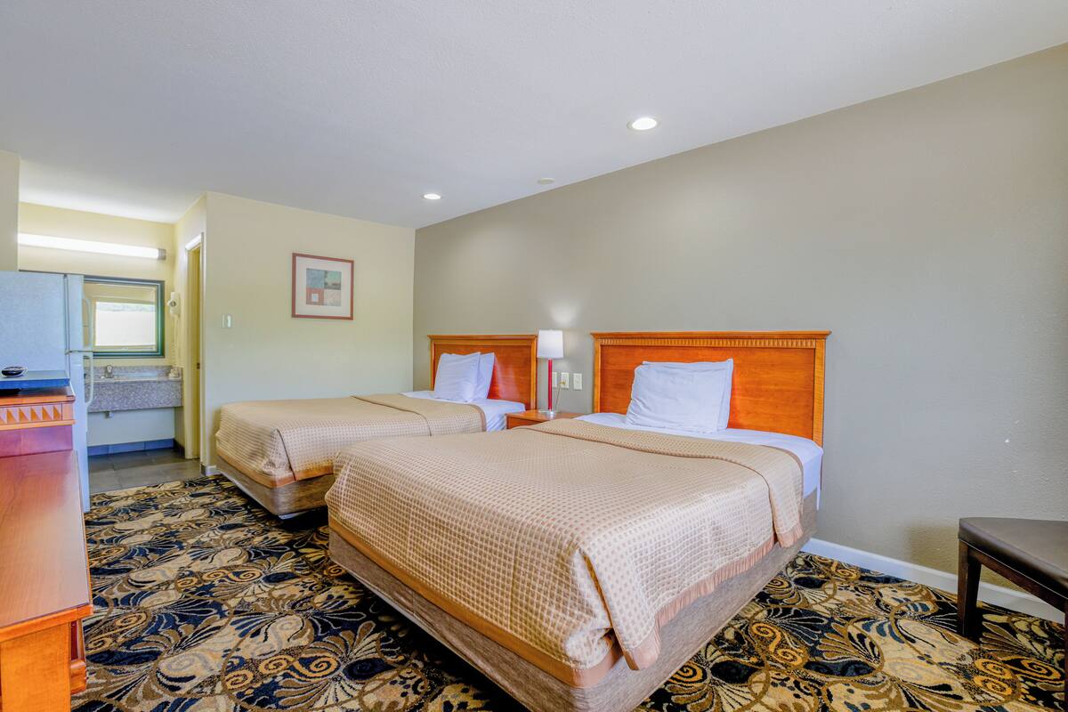 A hotel room with two beds, a desk, a chair, and a bathroom visible in the background.