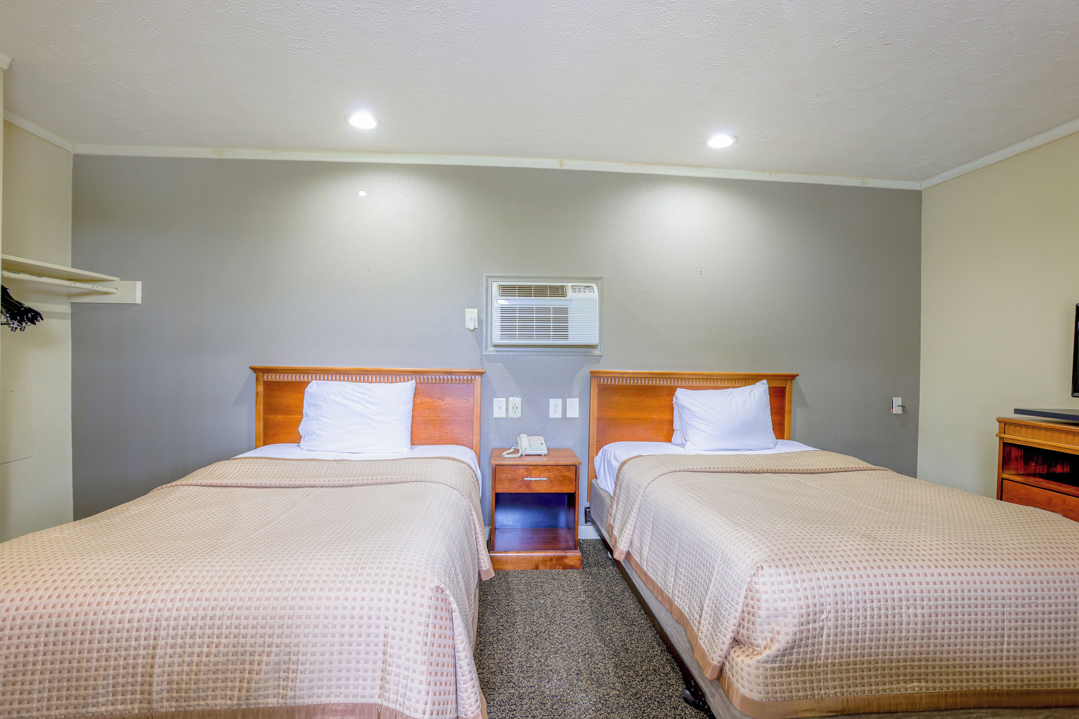 Hotelkamer met twee bedden, een klein nachtkastje met telefoon, een airconditioner en een televisie op een houten dressoir.