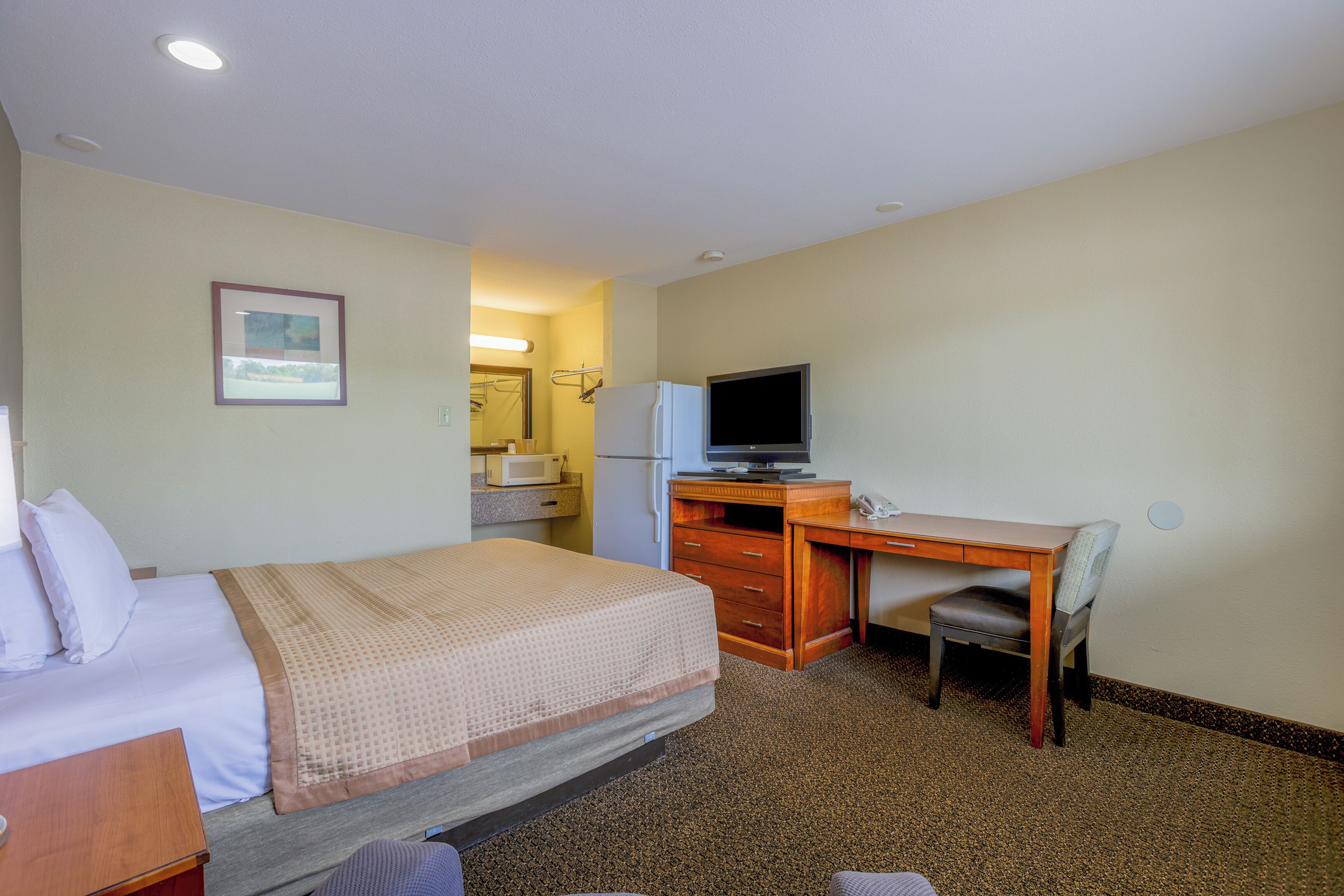 A hotel room with a bed, a desk, a chair, a television, and a bathroom visible in the background.