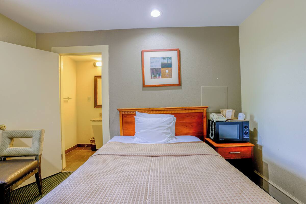 A hotel room with a bed, a chair, a nightstand with a microwave, and a framed picture on the wall.