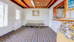 A hotel lobby with a patterned carpet, wooden ceiling beams, a reception desk with brochures, and a framed picture on the wall. - Budget Inn By OYO Natural Bridge I-81 (Natural Bridge)