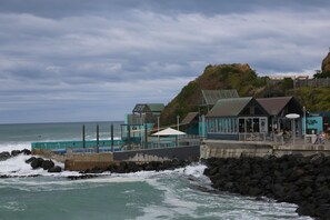 A coastal building with a pool, a rocky shoreline, and a cliff.