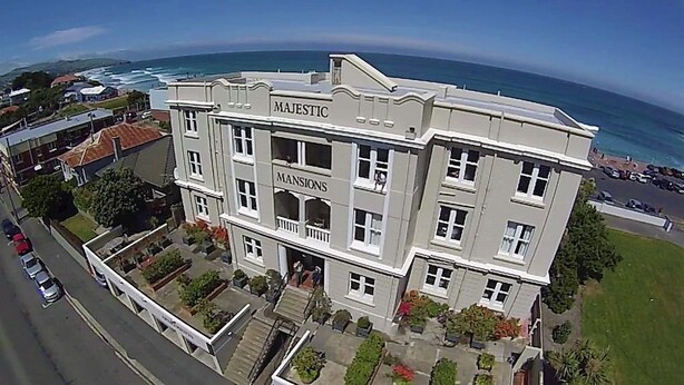 A large, multi-story building with the name "MAJESTIC MANSIONS" on its facade, located near a coastal area with visible ocean views. - Majestic Mansions - Apartments at St Clair (Dunedin)