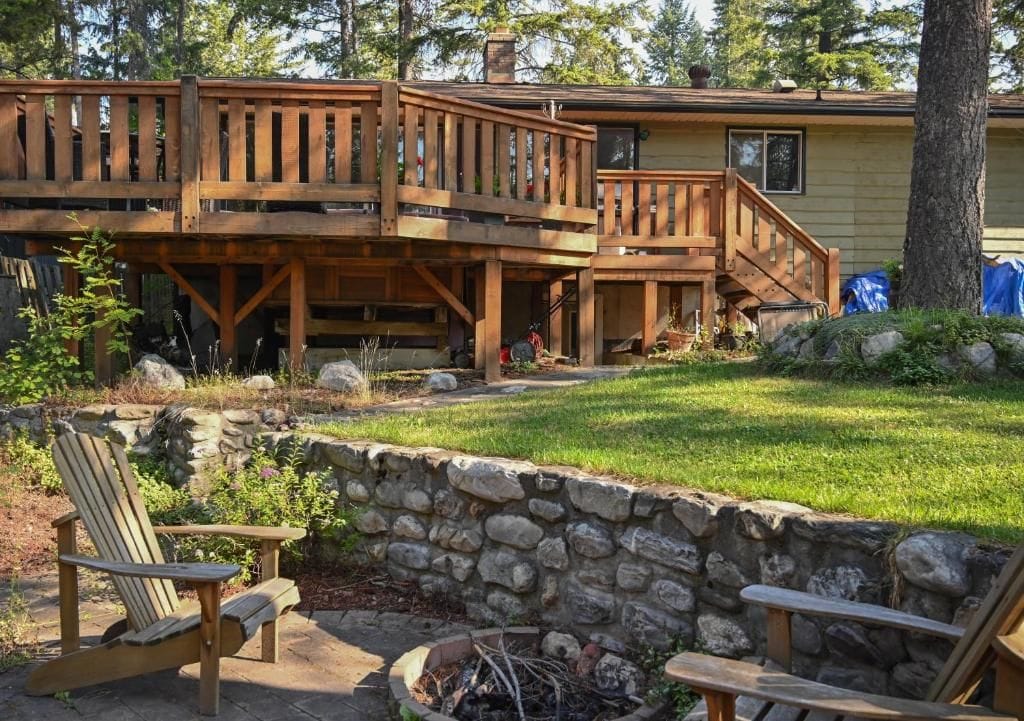 A wooden deck with a stone wall and two Adirondack chairs.