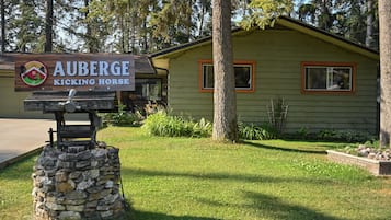 Un letrero de madera para 'Auberge Kicking Horse' con base de piedra, frente a un fondo de árboles y un edificio pequeño.