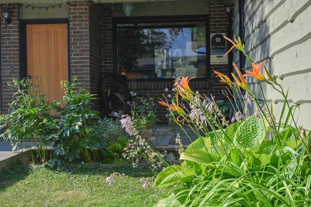 A brick building with a wooden door, a window with a sign, and a garden with various plants.