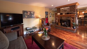 Una sala de estar con una televisión de pantalla plana, chimenea, comedor y cocina al fondo.