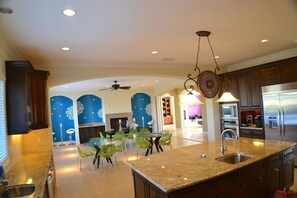 A spacious kitchen with granite countertops, stainless steel appliances, and a dining area with green chairs.