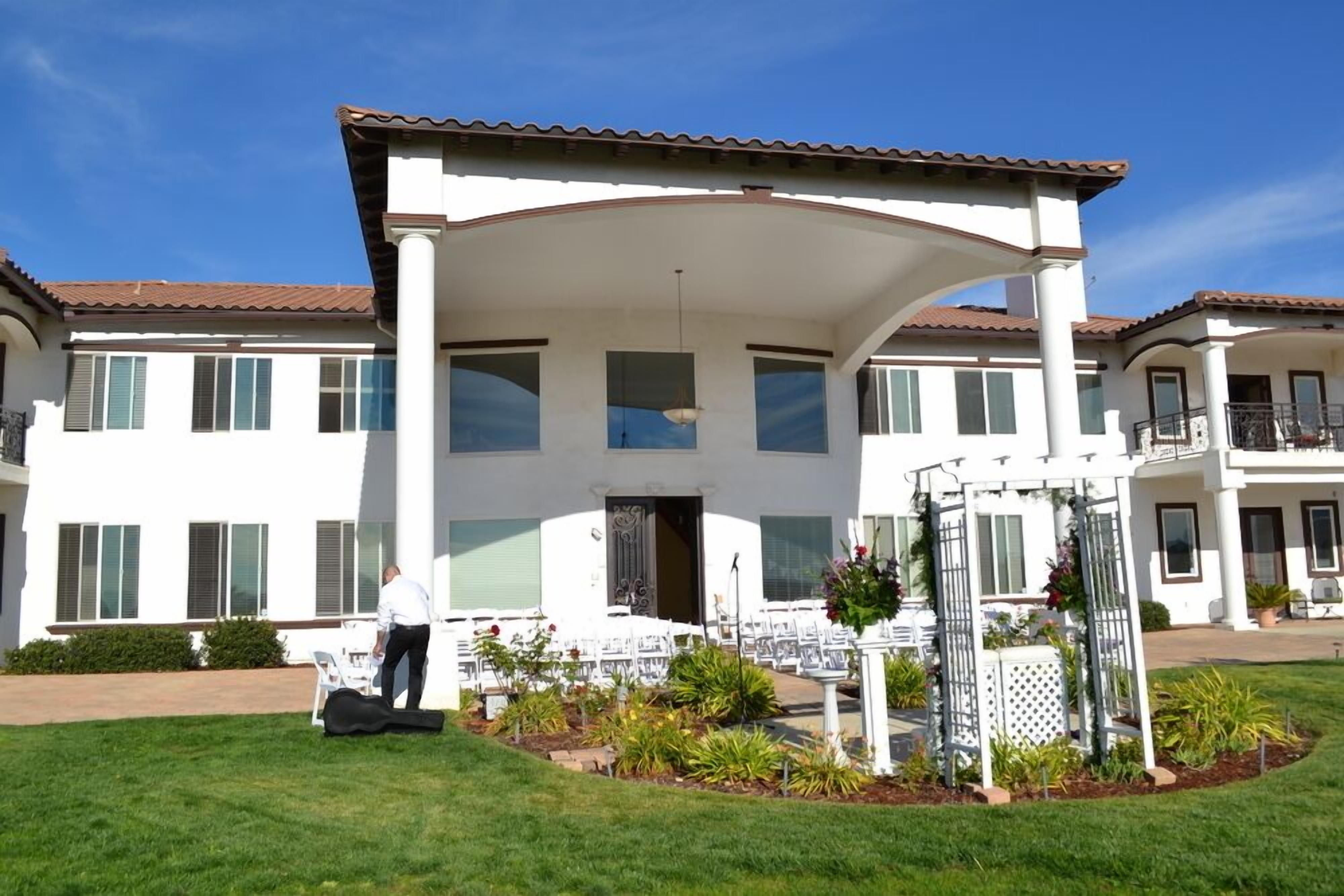 A large, two-story building with a covered patio area, multiple windows, and a well-maintained lawn.