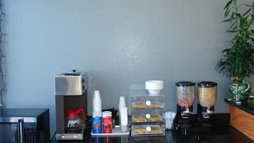 Una kitchenette con microondas, cafetera y diversos alimentos sobre la encimera.