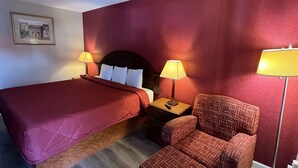 A hotel room with a large bed, two bedside lamps, a nightstand, a chair, and a framed picture on the wall.