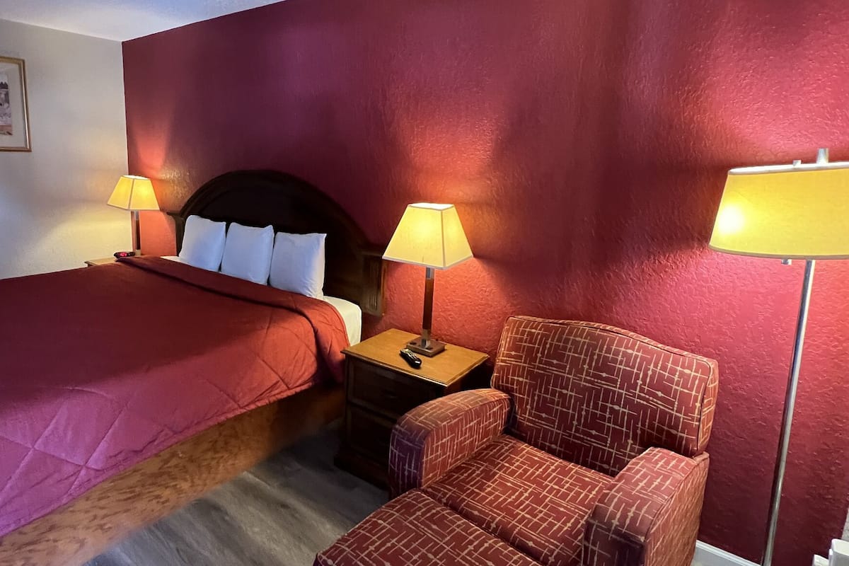 A hotel room with a large bed, two bedside lamps, a nightstand, a chair, and a framed picture on the wall.