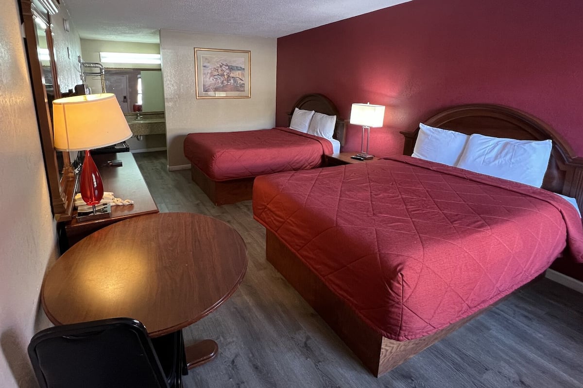 A hotel room with two beds, a desk, a chair, and a small table.