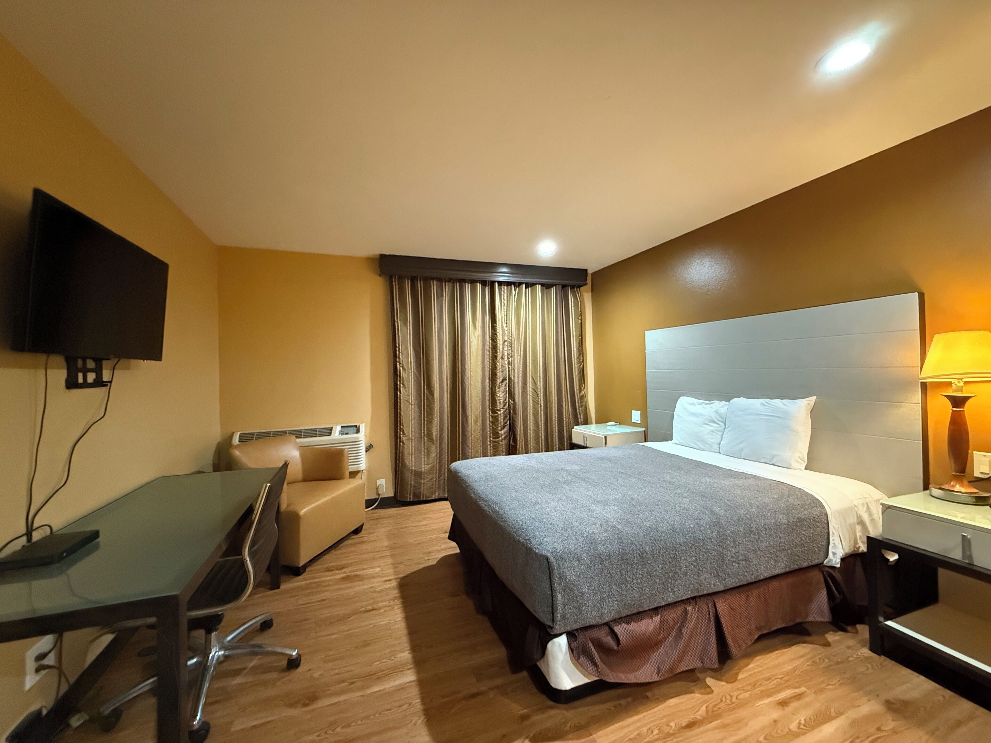 A hotel room with a bed, desk, chair, TV, and curtains.