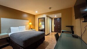 A hotel room with a bed, bedside tables, a desk, a chair, a TV, and a door.